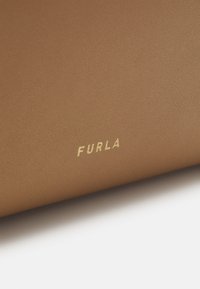 Pruun tekstuuriga nahk, millel on õrn puidust viimistlus. Kuldse reljeefse "FURLA" logo silmapaistvalt esitatud. Disain on minimalistlik ja elegantne.