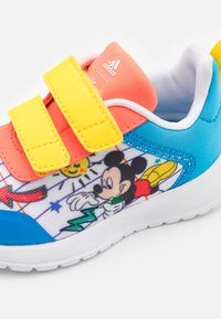 Zapatillas Adidas para niños con correas amarillas, talón azul y gráfico de Mickey Mouse sosteniendo un rayo verde en el lateral.