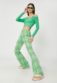 Zielony prążkowany crop top z wycięciami na ramionach; zielone spódnice w kształcie dzwonu w wzory; masywne białe sandały na platformie; zielone prostokątne okulary przeciwsłoneczne.