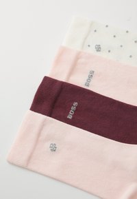 Vier Paar Socken: weiß mit Punkten, hellrosa, dunkelrosa und burgunderrot. Strukturierter Strick mit Logo-Akzenten in Silber.