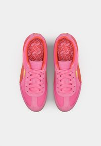 Lyserøde sneakers med en kombination af glatte og strukturerede materialer, med en lys orange accent og mønstret indersål.