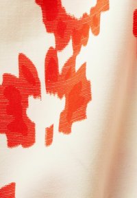 Tela de algodón con un patrón de grandes formas florales abstractas rojas sobre un fondo crema. Textura suave con un ligero brillo.