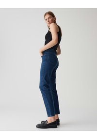 Jean en denim bleu foncé avec une coupe droite, design à cinq poches et détails cousus. Assorti à un débardeur noir et des mocassins.