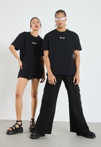 Černé oversized trička s bílým japonským textem, zkombinovaná s černými cargo kalhotami a sandály na platformě, které mají texturovanou gumovou podrážku.