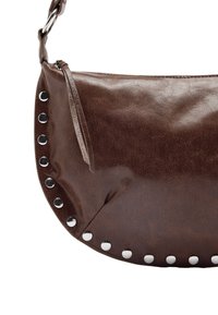 Brązowa torebka na ramię z syntetycznej skóry o zaokrąglonym kształcie, z metalowymi ćwiekami wzdłuż jednej krawędzi i zapięciem na zamek u góry.