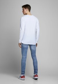Fehér hosszú ujjú ing, világoskék skinny farmerral párosítva. Fehér sportcipő piros és kék kiegészítőkkel. Egyszerű, hétköznapi öltözet sima textúrával.