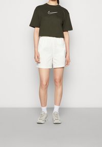 Green cropped Nike t-shirt, white lightweight shorts, white socks, gray sneakers. Simple design with embroidered logo on shirt and elastic waistband.