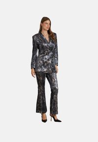 Samtanzug in Schwarz und Grau mit Marmor-Muster, bestehend aus einem zweireihigen Blazer und weit geschnittenen Hosen, kombiniert mit schwarzen High Heels.