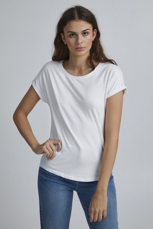 White short-sleeve t-shirt in soft fabric, with a round neckline and rolled cuffs, paired with blue jeans. Simple design and smooth texture.