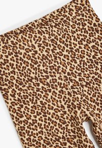 Leggings à imprimé léopard avec un fond beige, présentant un tissu texturé et côtelé avec des taches brunes, conçus avec une taille haute.