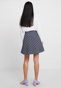 Una falda navy con un patrón circular, que presenta un diseño acampanado. La modelo lleva una blusa blanca de manga larga y unos zapatos púrpuras de tacón bloque.