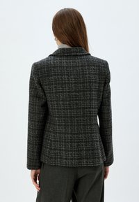 Blazer in donkergrijs tweed met een ruitpatroon, enkelgebroken ontwerp en geknipte revers. Heeft een aansluitende pasvorm en lange mouwen.