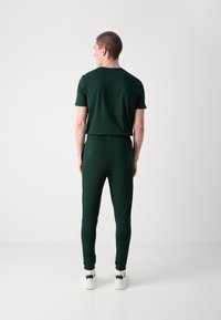 Mørkegrønn matchende T-skjorte og joggebukser, laget av et glatt stoff. T-skjorten har en klassisk rund hals; joggebuksene har en tettsittende silhuett.