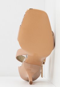 Nud patentläder högklackad sandal med en smal klack, texturerad sula och två ankelremmar, med en ormtryckt accent på sidorna.