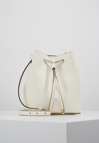 Krémová kožená kabela ve tvaru vědra s tahem na stáhnutí a nastavitelným popruhem, umístěná na bílé podstavě na bílém pozadí.