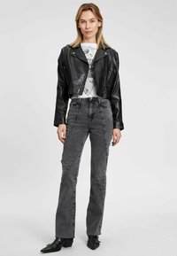 Schwarze, cropped Lederjacke mit Reißverschluss an der Vorderseite und glatter Textur, kombiniert mit grauen, hochtaillierten Jeans mit Nähten und ausgestellten Beinen.