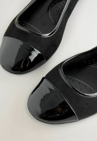 Svarta ballerinas med en mockakropp och glänsande lackad tå. Rundad form, med en strukturerad innersula och slät finish.