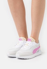 Sneakers bianchi con accenti rosa e crema, dotate di una tomaia in tessuto testurizzato, chiusura a lacci e una spessa suola bianca con trazione.