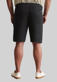 Zwarte linnen shorts met een rechte snit, voorzien van achterzakken, een tailleband en een lichtgerafeld zoom. Gekleed met witte sneakers.