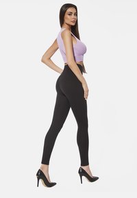 Czarne legginsy z wysokim stanem w połączeniu z jasnofioletowym topem bez rękawów. Top ma prążkowaną teksturę, a legginsy gładkie wykończenie.
