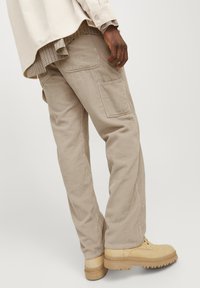 Beige corduroy pants with side pockets, straight-fit design, textured fabric, worn with a light shirt and tan shoes.
