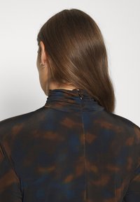 Hihna blusa med hög volangkrage i en blandning av bruna, blå och svarta nyanser; bakre stängning med en liten metallkrok.