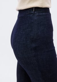 Σκούρο μπλε τζιν slim-fit με ψηλή μέση, με ομαλή υφή και διακριτικές ραφές κατά μήκος των πλαϊνών ραφών.