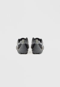 Grijze sneakers met een gestructureerd ontwerp, voorzien van een zwart accent, rubberen spikes op de zool en een achterste lus voor gemakkelijk aantrekken.