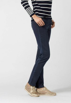 Navyblauwe jeans met een recht gesneden pijp, gecombineerd met metallic gouden sneakers met gestructureerde accenten en veters, gedragen met een gestreepte top.