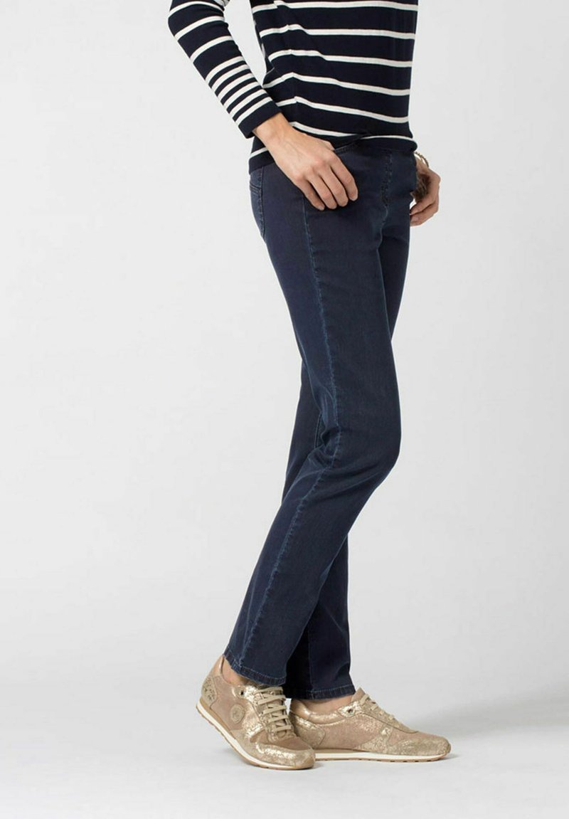 Jeans blu navy con taglio dritto, abbinati a sneakers oro metallizzato con accenti testurizzati e lacci, indossati con una maglietta a righe.