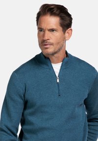 Donker teal pullover trui met een kwart-rits kraag, gemaakt van een zachte, gestructureerde stof. Voorzien van een contrasterende rits voor extra detail.