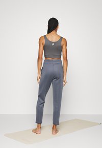Graues, kurz geschnittenes Tanktop mit Logo auf dem Rücken, kombiniert mit hoch taillierten grauen Jogginghosen. Glatte Textur, passgenauer Schnitt und minimalistischer Stil.
