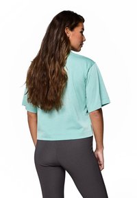 Miętowa crop top z krótkimi rękawami, gładka w dotyku, w luźnym fasonie, w połączeniu z szarymi legginsami. Brak widocznych wzorów lub akcentów.