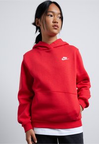 Hanoracul roșu Nike are o buzunar frontal tip pouch și manșete cu nervuri. Dispune de o glugă cu şnur și un logo alb pe piept. Textură de țesătură moale.
