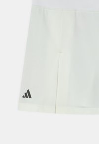 Falda atlética blanca hecha de una tela suave, con una cintura plana, diseño dividido y un logo de Adidas negro en el dobladillo izquierdo.