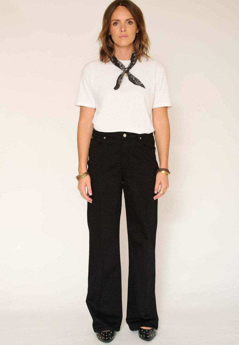 T-shirt blanc à manches courtes associé à un pantalon noir taille haute à jambes larges. Une écharpe noire avec un motif blanc accessoirise la tenue.