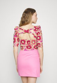 Top com estampa floral em rosa e amarelo, com mangas bufantes e design de costas cruzadas, combinado com uma saia rosa ajustada. Textura suave.