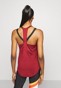 Sportieve tanktop in dieprood met zwarte bandjes, voorzien van een mesh rug en een comfortabele pasvorm. Gebogen zoom en atletisch ontwerp, geschikt voor sportkleding.