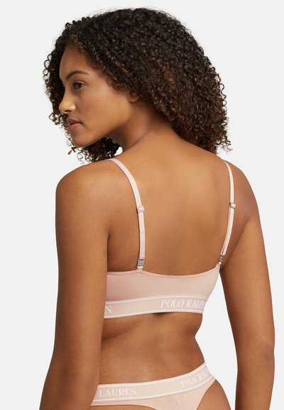 Bralette rosa claro con tirantes ajustables, textura suave y banda con logo blanca. Diseño sencillo que ofrece una cobertura mínima.