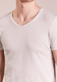 Světle šedé, krátké rukávy, tričko s výstřihem do V vyrobené z měkké látky. Má hladký povrch s minimálním šitím a bez viditelných vzorů.