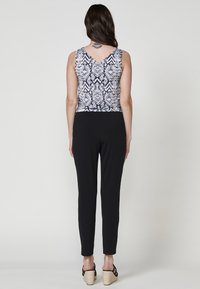 Pantaloni neri aderenti con un top senza maniche a manica larga con scollatura a V. Il top ha un design astratto in bianco e nero e una vita aderente.