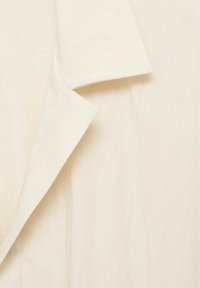 Cream, lightweight fabric with a smooth texture. Features a pointed collar and visible stitching accents. Simple and minimalistic design.