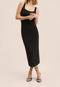 Robe noire longueur genou avec larges bretelles et encolure dégagée, en tissu extensible. Présente une silhouette ajustée et une texture lisse.