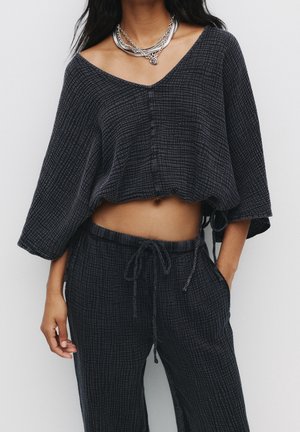 Gekürztes, dunkelgraues, strukturiertes Oberteil mit V-Ausschnitt und weiten Ärmeln, kombiniert mit locker sitzenden, mit Kordelzug versehenen Hosen aus demselben Stoff.