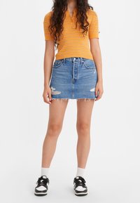 Gul randig pikétröja med korta ärmar, kombinerad med en ljusblå denim minikjol med slitna detaljer och fransar i nederkant. Svarta sneakers.