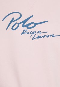 Ljusrosa sweatshirt med en blå kursiv logo som säger "Polo Ralph Lauren." Tyget verkar mjukt med en slät textur.