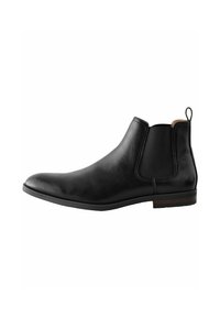 Bota Chelsea de cuero negro con paneles laterales elásticos, textura suave, punta redondeada y un acento marrón en el talón.
