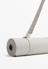 Siva mat za jogo v sivi barvi, zavit in zaklenjen z ujemajočim trakom, ki ima teksturirano površino in krožno konico s ravnim robom.