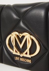 Black quilted leather bag with gold interlocking heart and "M" logo and "LOVE MOSCHINO" text on front.