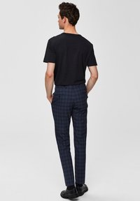 Camiseta negra combinada con pantalones de cuadros oscuros en azul marino y gris, con un corte ajustado, bolsillos y zapatos negros de punta cerrada.